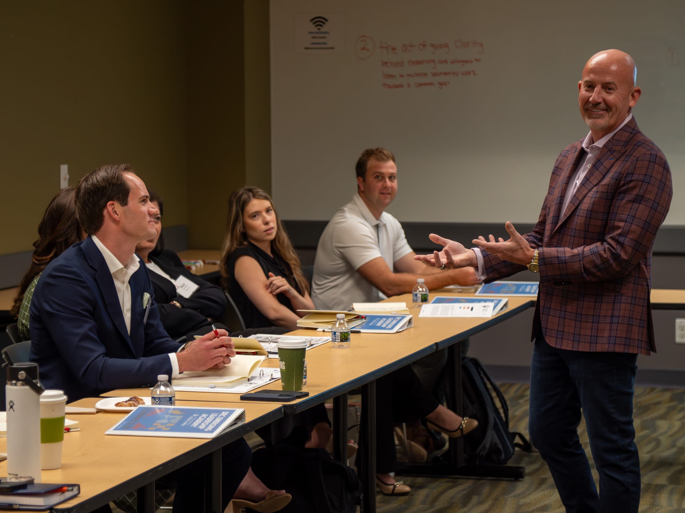 Steve Lowisz teaching a leadership workshop, mid-gesture, with an engaged room of hiring leaders around the table